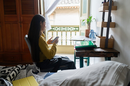 Young woman using phone sitting by window at home