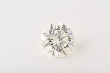 Fototapeta premium A sparkling diamond rests on a plain white surface, catching light with its brilliant facets.