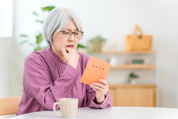 家で年金手帳を見ながら困る,悩むシニア女性