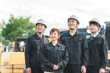 Male and female construction and building workers in work clothes in front of heavy machinery