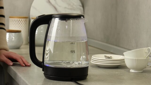 Woman turning off electric kettle at countertop in kitchen, closeup