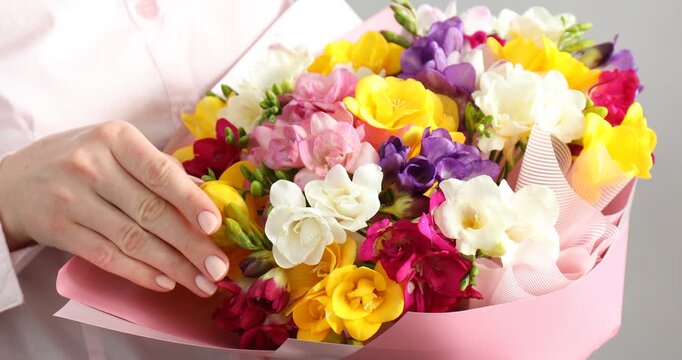 Woman with bouquet of colorful freesia flowers on grey background, closeup