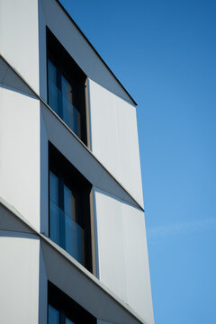Geometric white facade of a modern building with large windows and sharp lines, set against a clear blue sky. Suitable for illustrating contemporary architecture, urban design, or real estate concepts