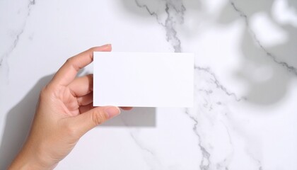Obraz premium Hand holding a blank white business card mockup on marble background