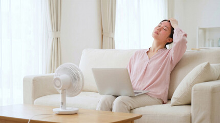 A distressed woman attempts to cool down with a small fan while working on her laptop.