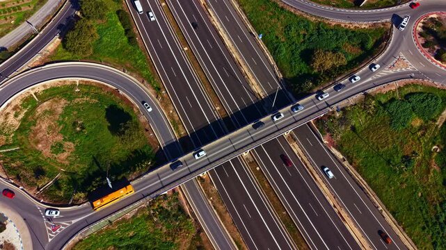 Cars move along highways and bridges in an urban area. The layout shows multiple lanes and an intersection where roads connect. Green spaces are nearby.