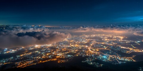 Fototapeta premium Breathtaking Night View of City Lights and Clouds from a High Mountain Peak Above the Landscape in a Clear Starry Sky