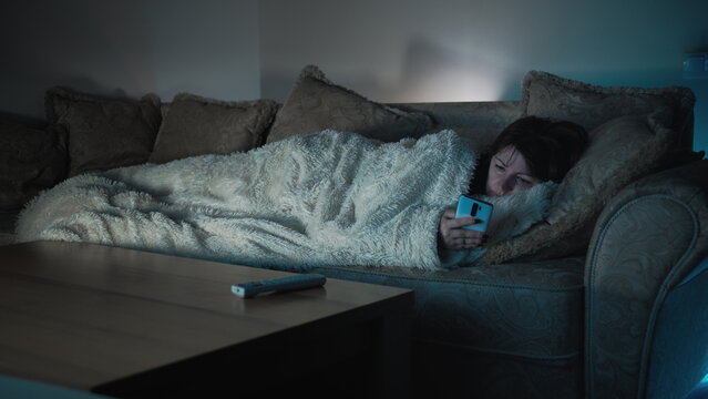 sad woman lies on the sofa in front of tv and uses the phone, have fun and enjoy