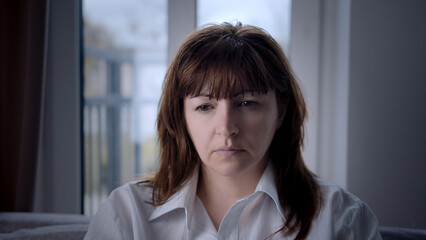 Thoughtful middle-aged woman indoors looking down, sad woman looking down thoughtfully, inner world