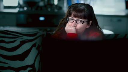 Woman Wearing Glasses Watching Screen at Home in Low Light, A woman watches TV with concern