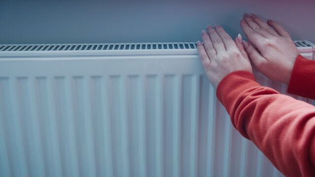 hands switching on the heating season close up, A woman tries to warm her hands on a radiator in winter