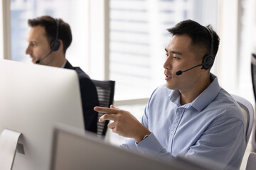 Customer support workflow. Focused young adult male hotline consultant salesman in wireless headset...