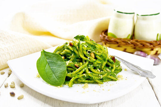 Spaghetti with spinach and pine nuts in plate on board