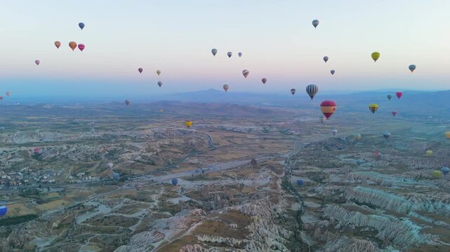 Goreme, Nevsehir, Turkey. Epic landscape of Cappadocia Red Valley with hot air balloon armada firing burners under dramatic morning sky. Aerial View
