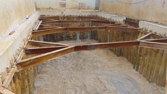 Deep excavation pit displaying a temporary horizontal steel shoring system with cross bracing providing earth retention and structural support for future building foundation construction