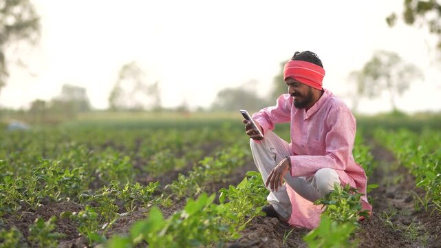 young indian farmer using smartphone sitting at agricultural field
