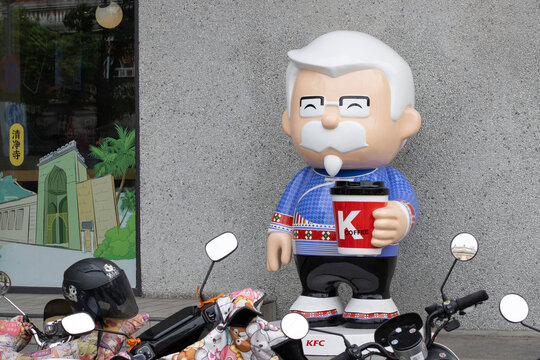 Quanzhou, Fujian, China - Apr 10, 2024: A statue of Colonel Sanders holding a KCOFFEE cup stands outside a KFC restaurant in downtown Quanzhou, Fujian Province, China.