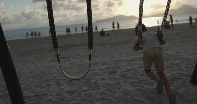 Boy swings on swingset on beach at sunset - wide shot