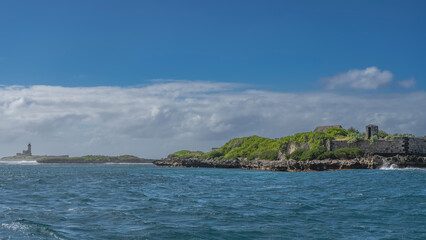 Islands in the ocean. An old lighthouse on a background of blue sky and clouds. Ruins of an old prison among the green vegetation. Mauritius. &Icirc;le aux Fouquets.  Prison Island
 