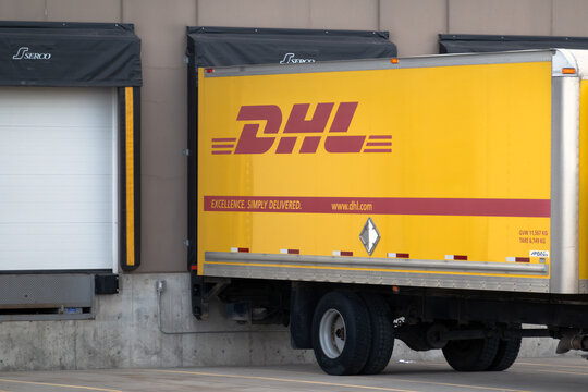 Calgary, Alberta, Canada. March 10, 2026. A bright yellow DHL delivery truck is backed into a concrete loading dock at a distribution warehouse.