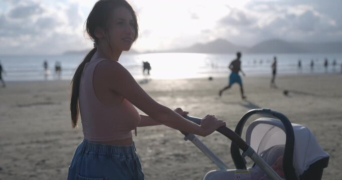 Young mom pushing stroller along beach on sunny summer day  while baby sleeps