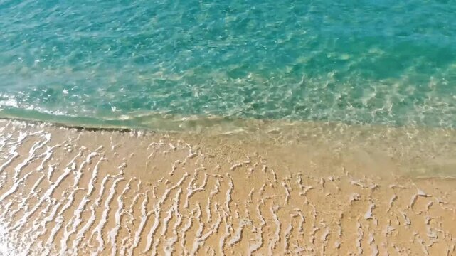 Gentle waves lapping on sandy beach shore with clear turquoise water