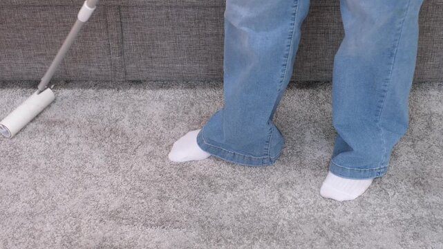 A woman removes dirt from a gray carpet using mop with lint roller.