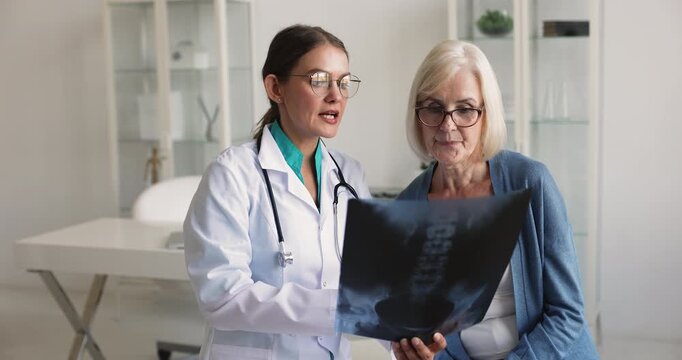 Doctor and middle age woman patient reviewing X-ray of spine, pelvis or lower back, explains joint conditions, degeneration or age-related changes, gives health recommendation during visit at hospital
