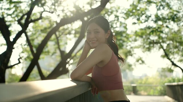 Portrait of a confident Asian woman athlete smiling in a green city park. Fit female enjoying outdoor fitness, fresh air and healthy lifestyle. Wellness, longevity and active living concept.
