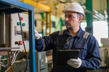 Obraz na płótnie Canvas Male industrial engineer holding digital tablet while operating control panel switch in manufacturing factory plant. Professional technician checking machinery system maintenance process