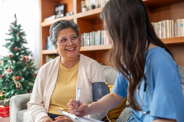 Happy senior Asian woman smiling while nurse checking blood pressure at home. Professional...