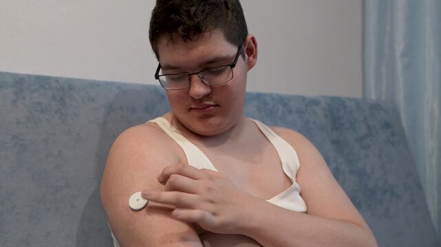 A young man attaches a glucose sensor to his arm for blood sugar monitoring, representing diabetes care and management.