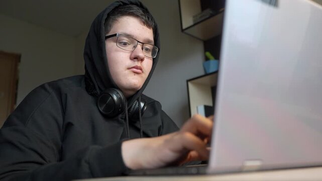 A serious, intense teenager types on a keyboard, programming or hacking into a system with focus and determination.