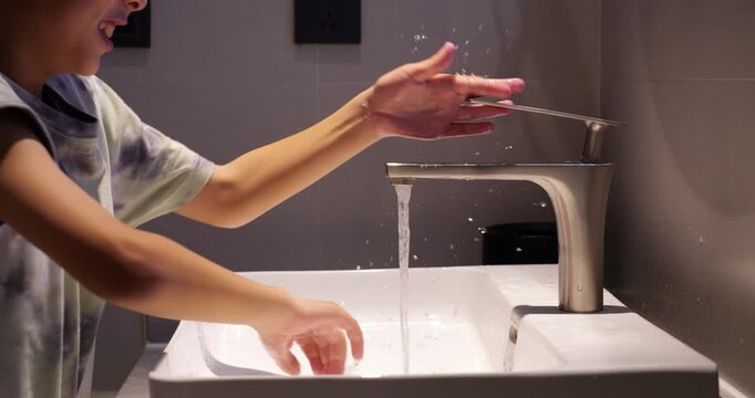 Capricious boy washes his hands with dissatisfied grimace on his face, quickly rubbing hands under stream of water from stylish mixer tap, then turns off tap and runs away. Side view, slow motion.