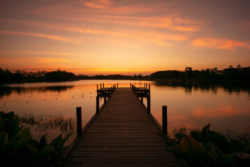 Obraz premium Wooden walkway into the lake with natural scenery of sunset and silhouette of forest in background