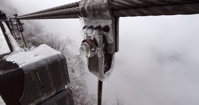 Close-up of steel cable clamp and hanger connection on Tianmen Mountain Suspension Bridge encased in glaze ice. Following sudden night storm in late March, bridge's rigging is covered with ice