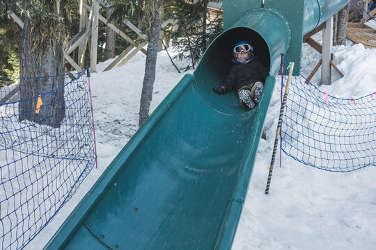 Young boy slides down a slide at a snow covered playground
