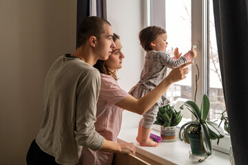 Obraz premium Parents and toddler looking out window at home, family bonding moment