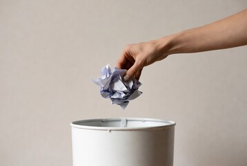 A hand is discarding a crumpled paper ball into a trash can. A simple, neutral background setting.