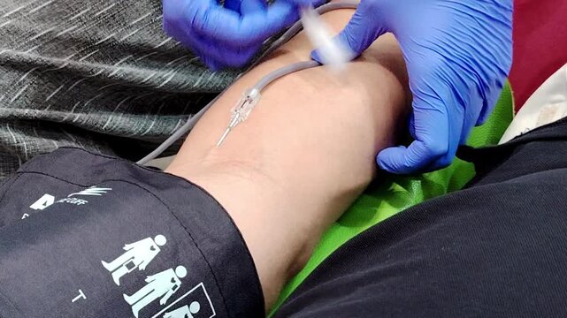 medical procedure where a clinician in blue gloves is preparing to insert a needle into a patient's arm.  This type of procedure is used for administering fluids, medications, or drawing blood.