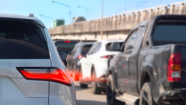Luxury white car with turn on brake light. Show effect speed light. Cars parked and queue along the highway of the road. Side of road with concrete overpass under blue sky.