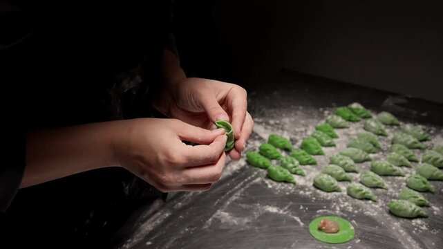 Close up of hands carefully shaping vibrant green dumplings on a floured surface, arranging handmade filled dough pieces in neat rows under soft side lighting