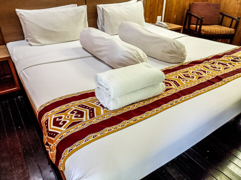 Comfortable hotel bed with traditional ethnic fabric runner in a wooden cabin room