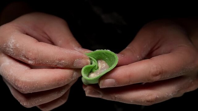 Close-up hands shaping bright green dumpling wrapper around creamy filling, detailed step-by-step folding process highlighting artisan handmade cooking technique