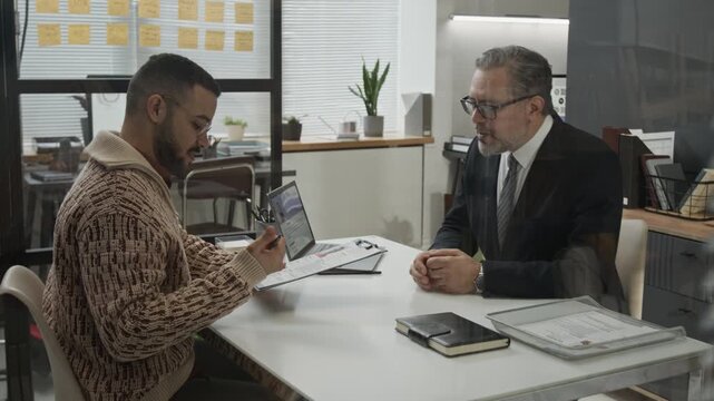 Gen Z man receiving application form from middle-aged male HR specialist and signing it after successfully going through job interview in modern office