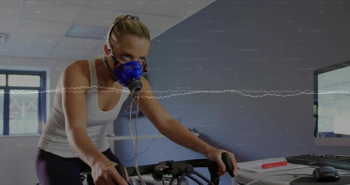 Woman pedaling on exercise bike after mask hookup showing waveform tracking breathing for testing