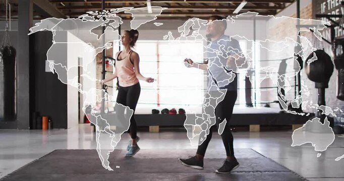 Workout partners gripping ropes, skipping in sync on mat in gym, world map overlaying for fitness