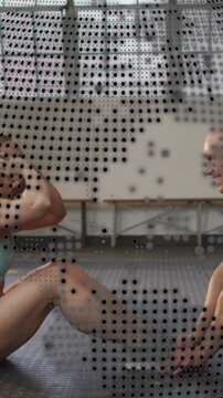 Vertical video: Left woman doing situps with man holding shoes and dotted overlay in gym for core
