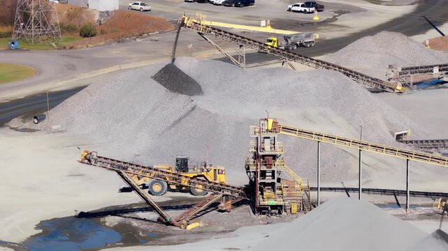 Front loader and conveyor system beside gravel piles at Jones Mill Quarry Arkansas USA, excavators and trucks drive through complex