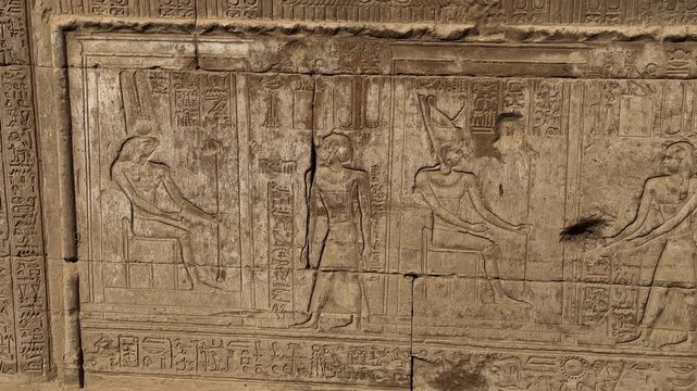 Detailed panning shot of ancient Egyptian stone reliefs and hieroglyphics on the walls of the Temple of Hathor in Dendera depicting pharaohs and deities in ritual scenes.